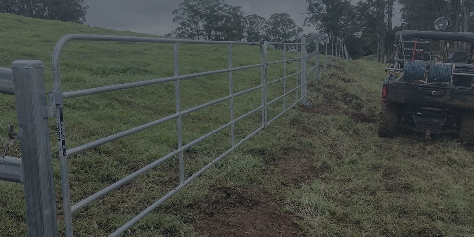 A galvanised pipe gate and fence line under a heavy sky