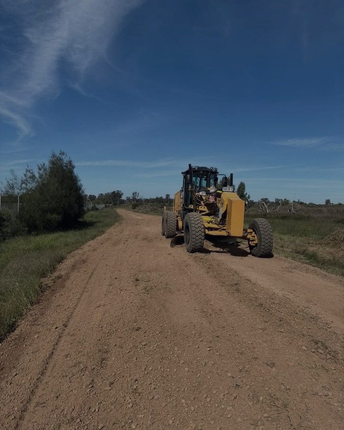 A grader clearing a red dirt line across the paddock