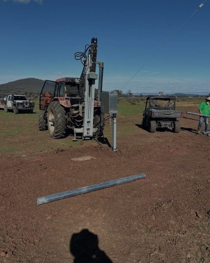 A post driver on the back of a tractor driving a steel strainer into the ground